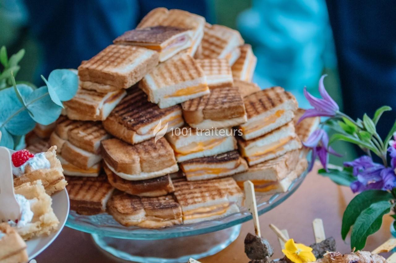 Plateau de sandwichs grillés empilés, garnis de fromage et de jambon, entouré de décorations florales.