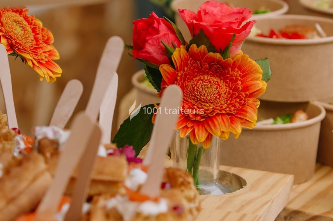 Bouquet de fleurs orange et rouges dans un vase en verre, entouré de plats en carton et de bâtonnets en bois.