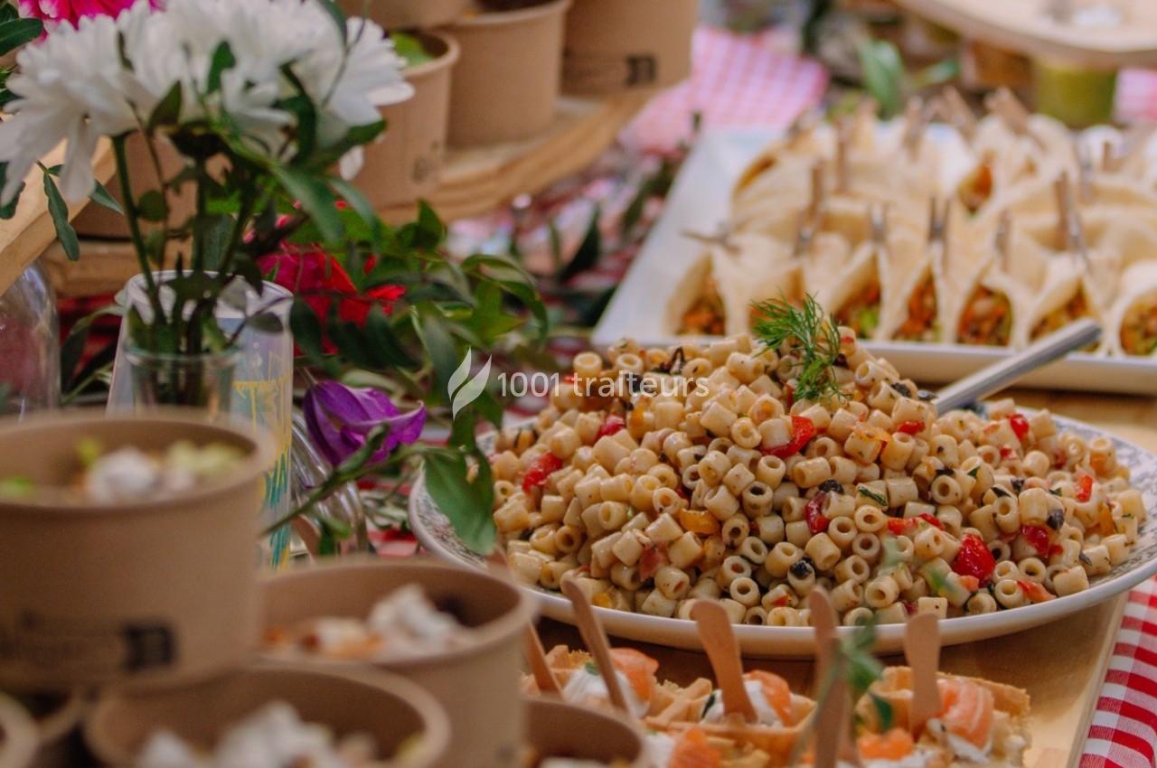 Buffet varié avec salade de pâtes, tacos, fleurs décoratives et autres plats sur une nappe à carreaux rouges et blancs.