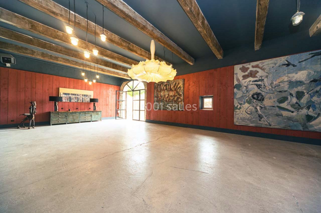 Salle spacieuse avec murs rouges, poutres apparentes, œuvres d'art accrochées et grande porte vitrée.