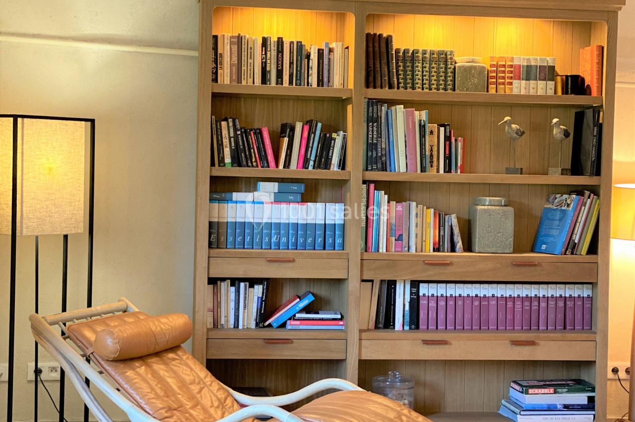 Bibliothèque en bois éclairée, remplie de livres, avec un fauteuil en cuir inclinable et une lampe dans un intérieur…