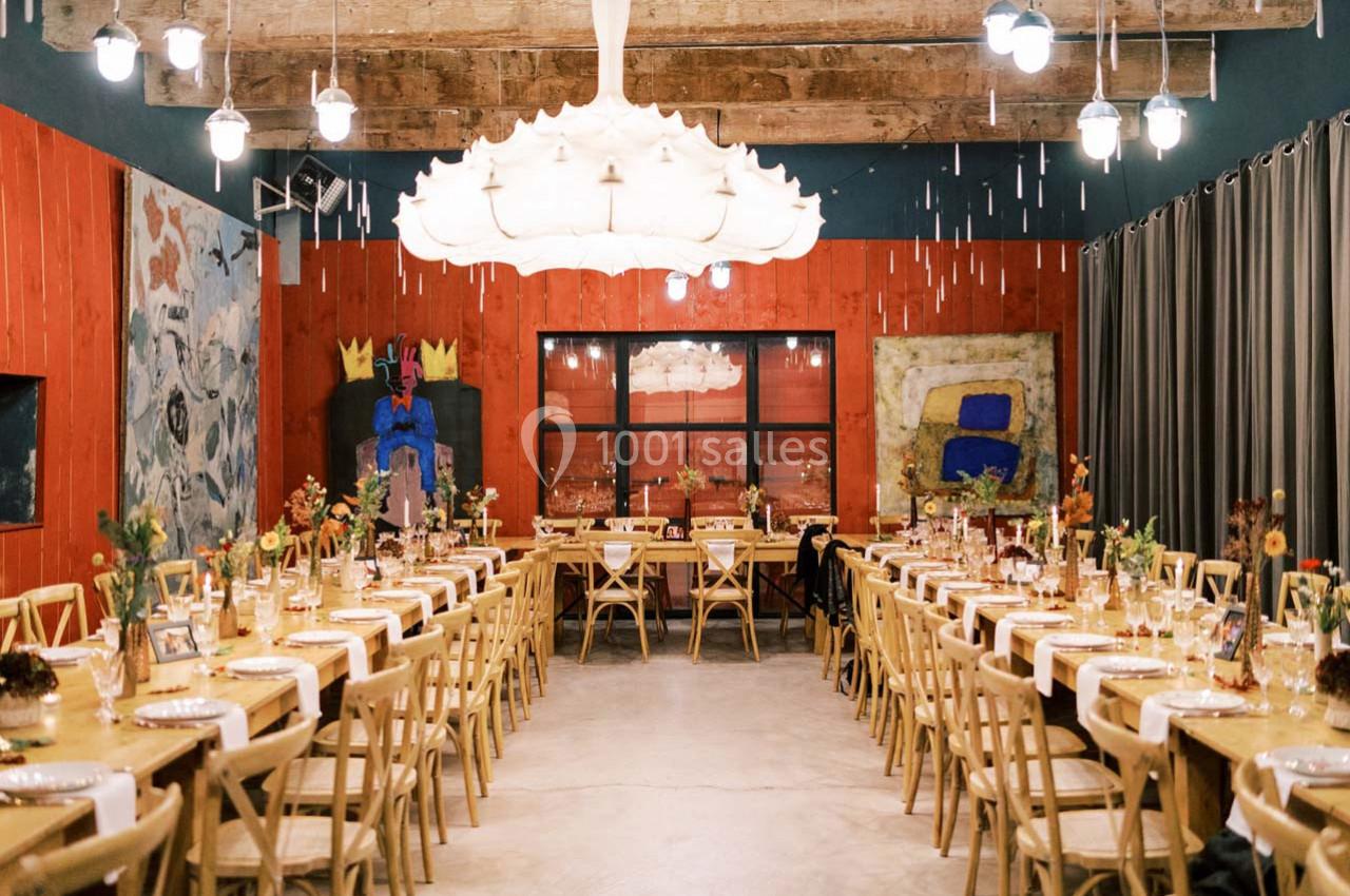 Salle de réception décorée avec des tables alignées, des chaises en bois, des fleurs et des œuvres d'art aux murs.