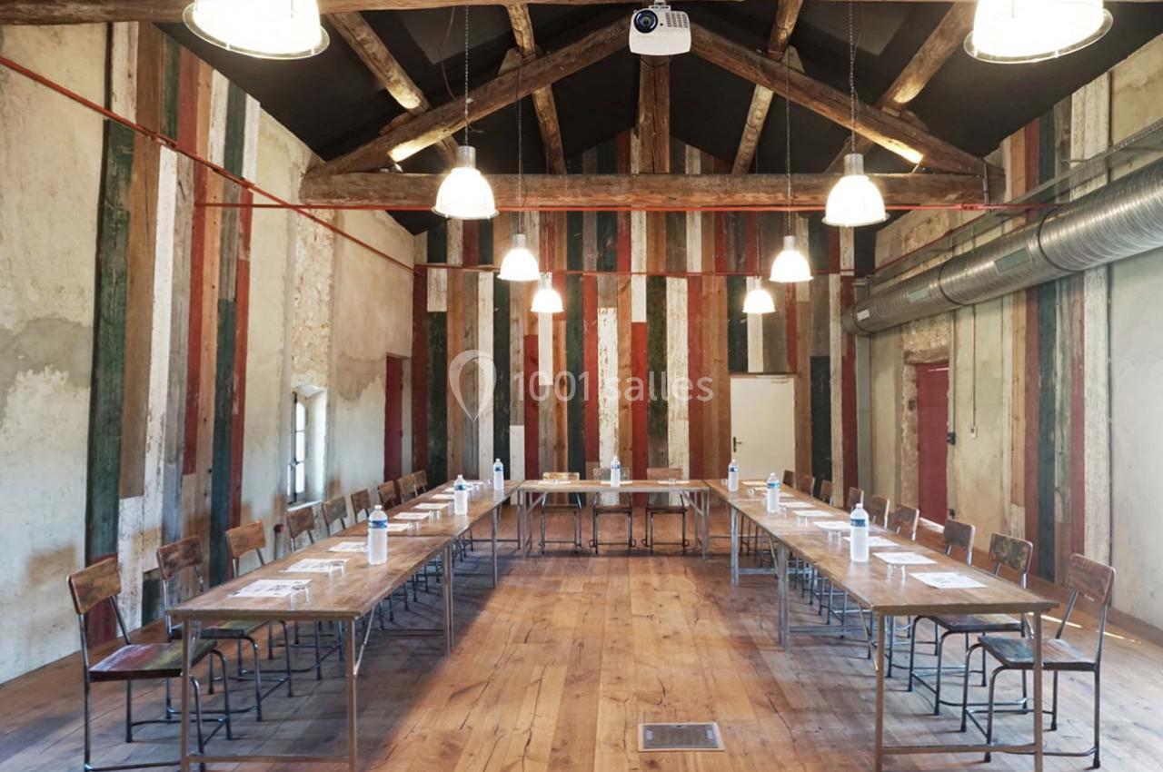 Salle de réunion rustique avec tables disposées en U, chaises en bois et murs en bois coloré.