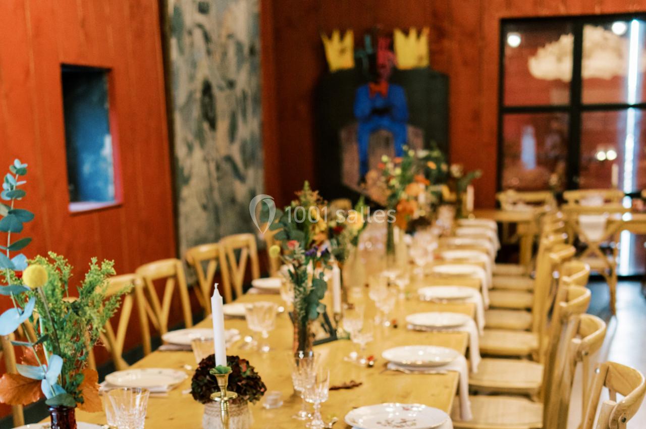 Salle de réception décorée avec des tables alignées, nappes blanches, bougies et arrangements floraux.