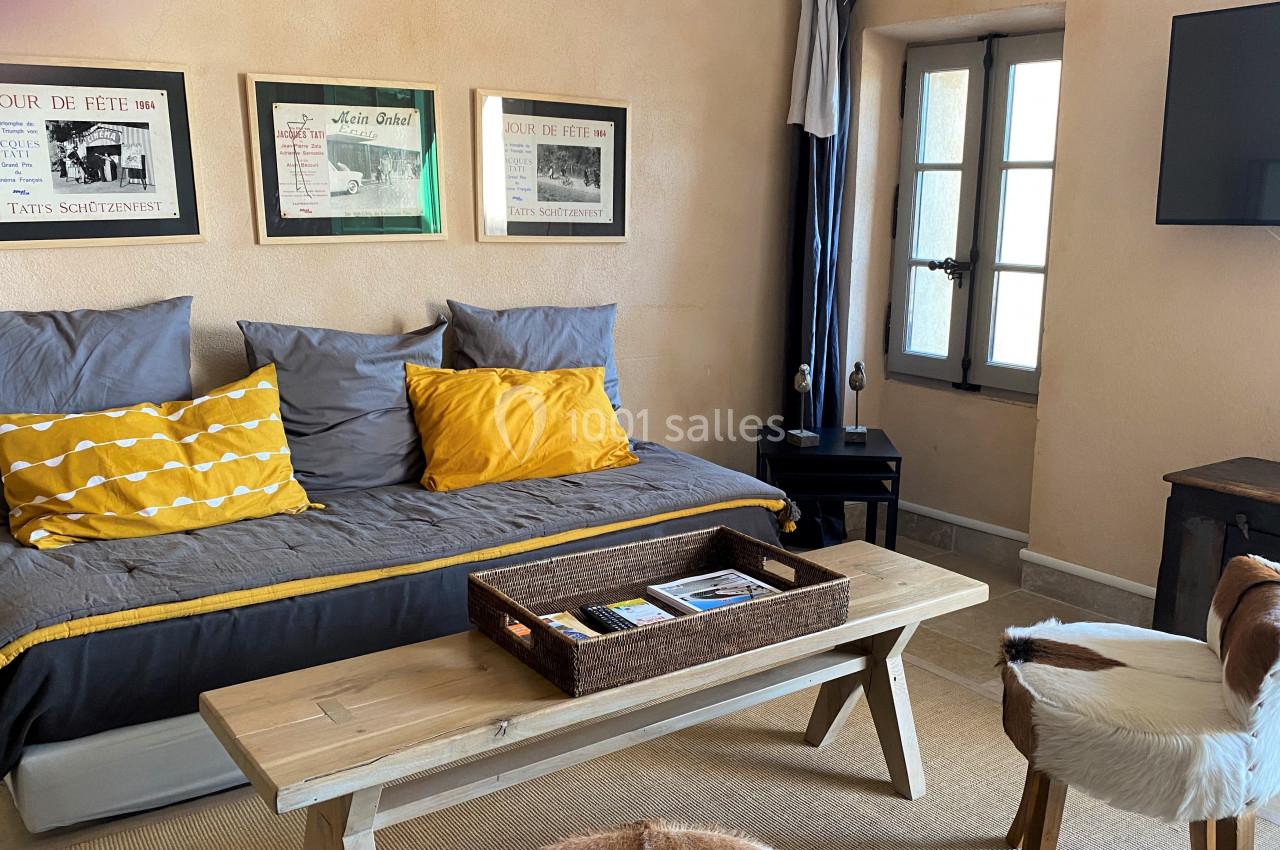 Salon lumineux avec canapé-lit, coussins jaunes, table basse en bois, chaises en peau et décorations murales.
