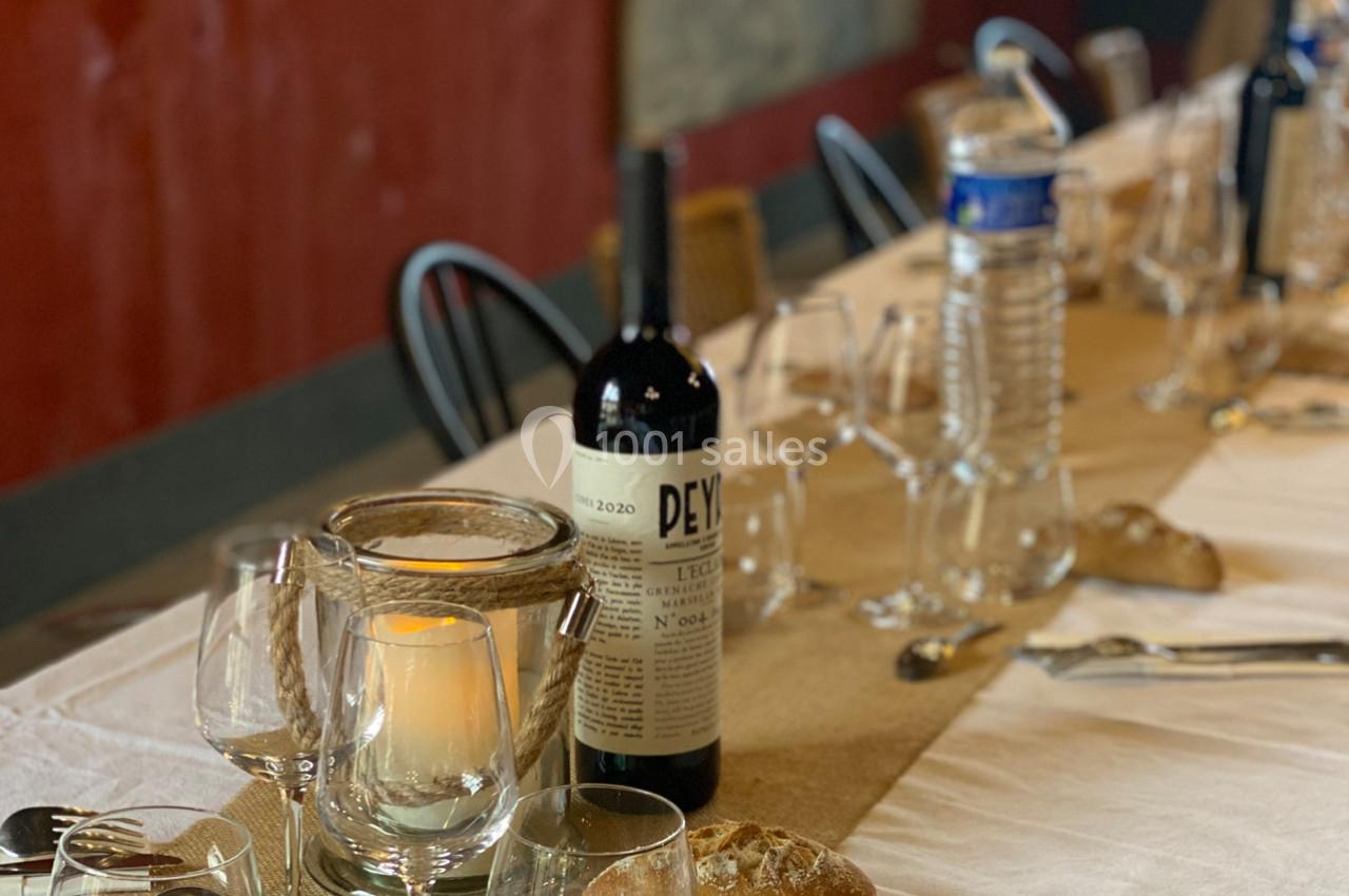 Bouteille de vin rouge, bougie allumée et verres disposés sur une table dressée avec nappe blanche et pain.