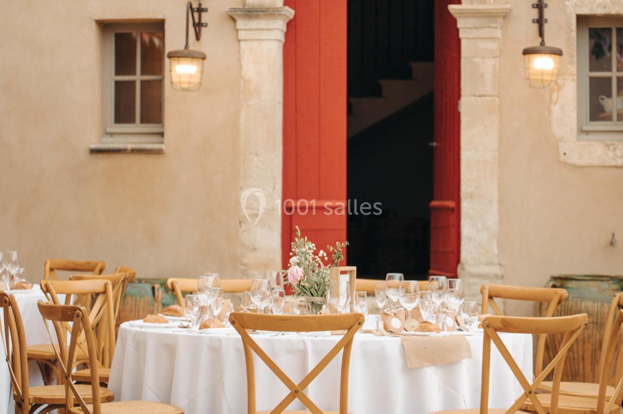 Table ronde dressée avec vaisselle élégante, entourée de chaises en bois, devant une porte rouge et des murs beige.