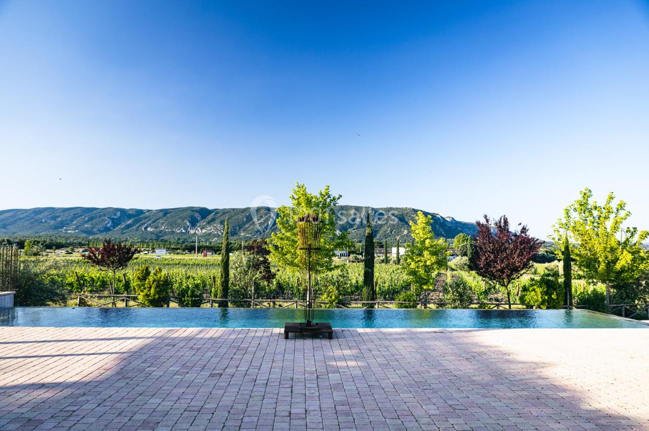 Vue sur une piscine à débordement entourée de végétation, avec des collines verdoyantes à l'horizon sous un ciel bleu.