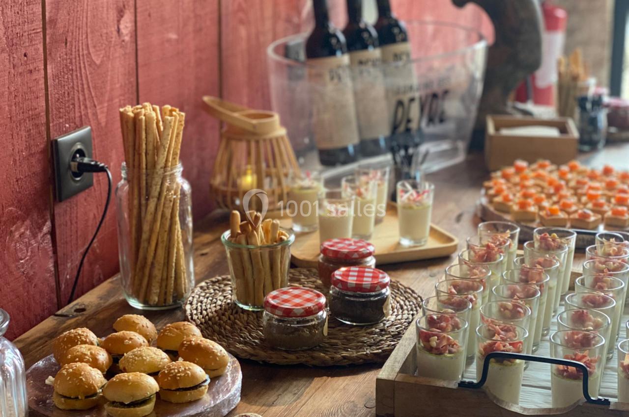 Buffet avec mini-burgers, verrines, gressins, pots de confiture et bouteilles de vin sur une table en bois.