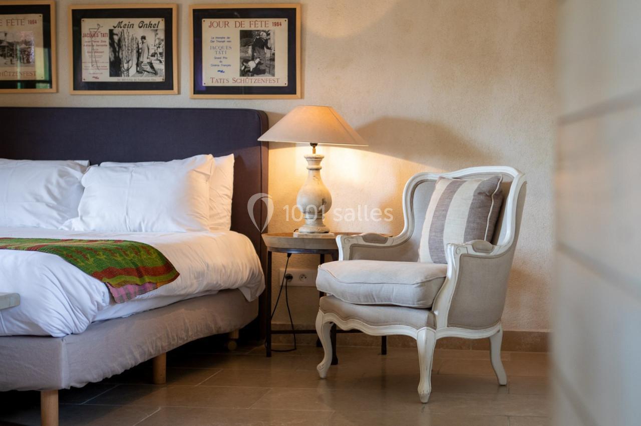 Chambre avec lit double, fauteuil, lampe de chevet et décorations murales sur un mur beige.