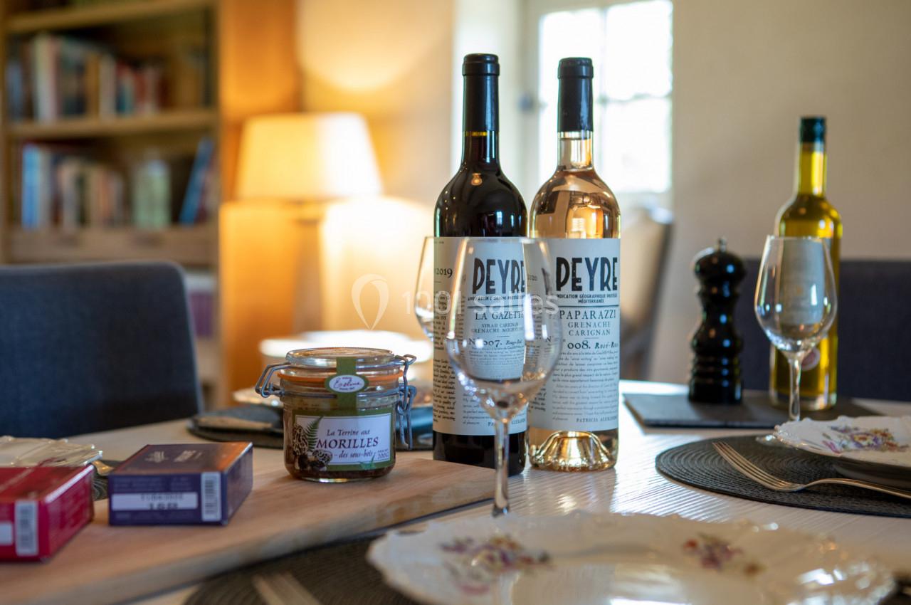 Bouteilles de vin, verres, pot de confiture et assiettes disposés sur une table dressée dans un intérieur chaleureux.