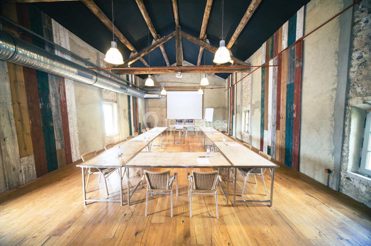 Salle de réunion lumineuse avec de grandes tables en bois, des chaises en osier et un écran de projection.
