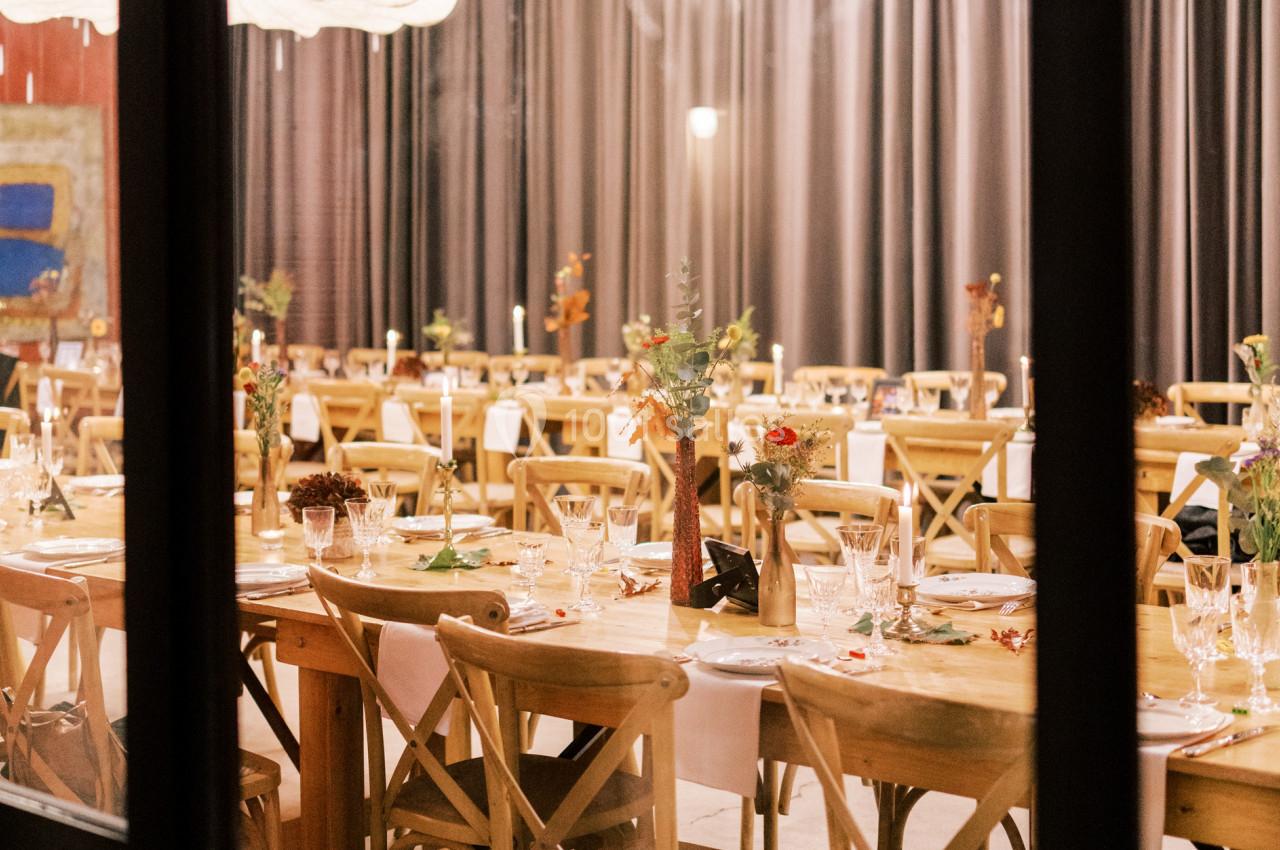 Salle de réception décorée avec des tables en bois, chaises assorties et centres de table fleuris, vue à travers une fenêtre.