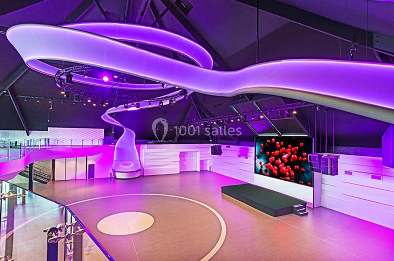 Salle moderne avec éclairage violet, écran géant affichant des sphères rouges et espace central circulaire.