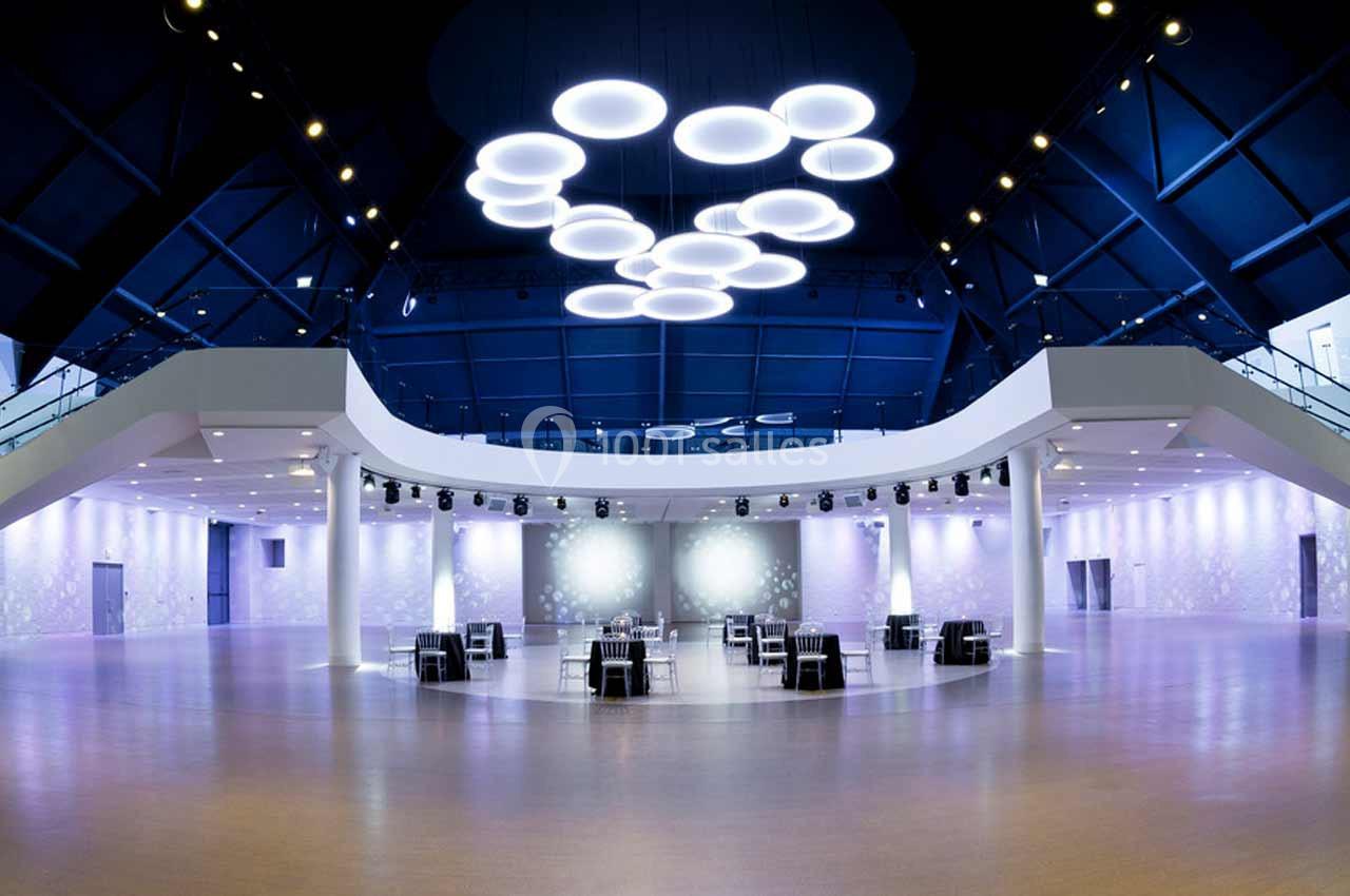 Salle spacieuse et moderne avec un plafond bleu, des luminaires circulaires suspendus et des tables dispersées.