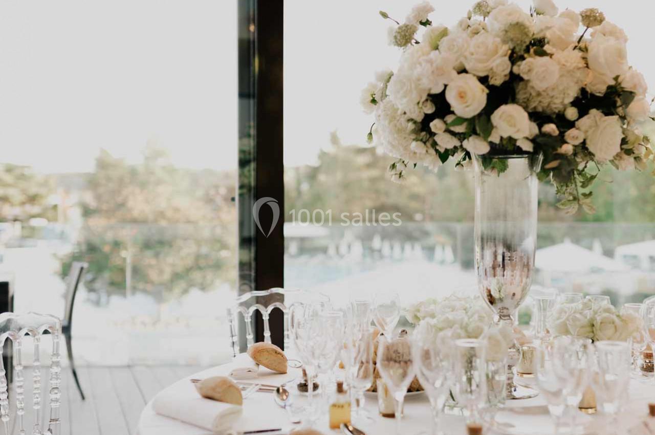Centre de table floral avec roses blanches et verdure, entouré de vaisselle élégante sur une table dressée.