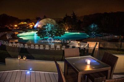 Piscine éclairée de nuit entourée de chaises longues, avec une terrasse en premier plan et des bougies allumées.