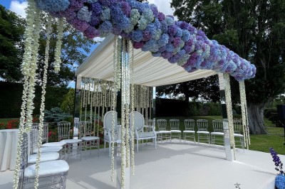 Terrasse ensoleillée avec tables noires dressées, parasols blancs et vue sur une piscine entourée de verdure.