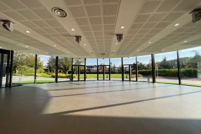 Terrasse ensoleillée avec tables noires dressées, parasols blancs et vue sur une piscine entourée de verdure.
