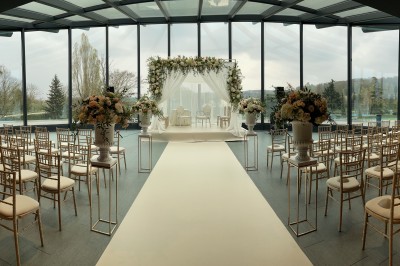 Terrasse ensoleillée avec tables noires dressées, parasols blancs et vue sur une piscine entourée de verdure.