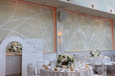 Terrasse ensoleillée avec tables noires dressées, parasols blancs et vue sur une piscine entourée de verdure.