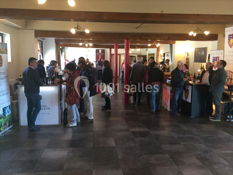 Des personnes dégustent du vin et discutent autour de stands dans une salle lumineuse au sol carrelé.