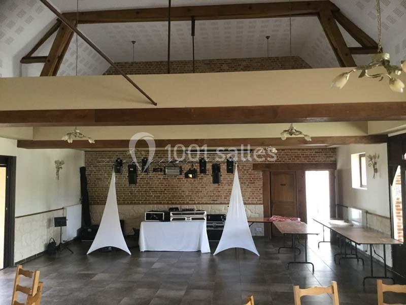 Salle de réception avec murs en briques, poutres apparentes, tables disposées et espace aménagé pour un équipement audio.