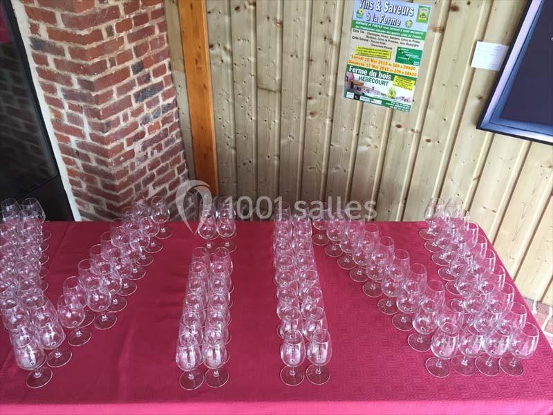 Rangées de verres à vin vides disposés sur une nappe rouge devant un mur en bois et une affiche.