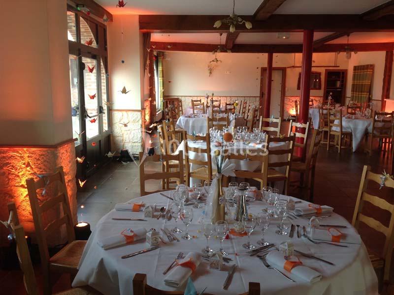 Salle de réception décorée avec des tables rondes dressées, éclairage chaleureux et pliages en papier suspendus.