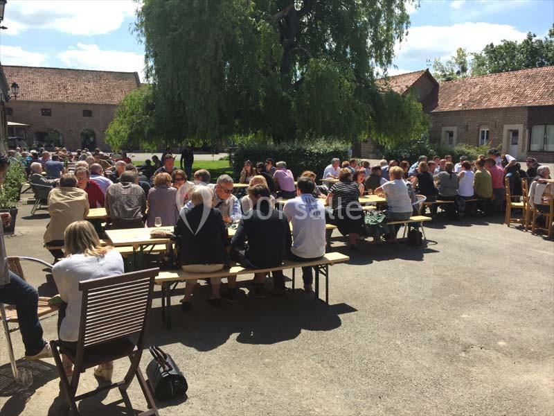 Des personnes assises à des tables en plein air dans une cour ensoleillée entourée de bâtiments en briques.