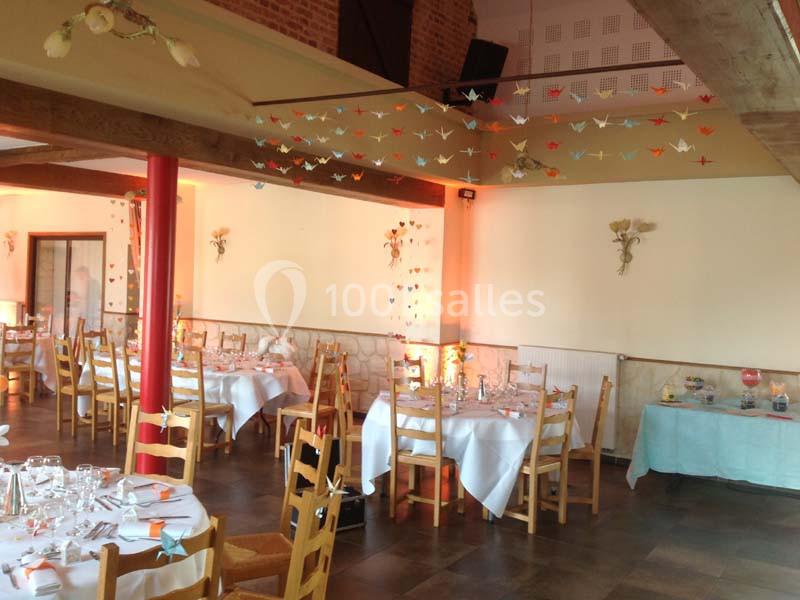 Salle de réception décorée avec des tables dressées, des guirlandes de grues en papier suspendues et une lumière chaleureuse.