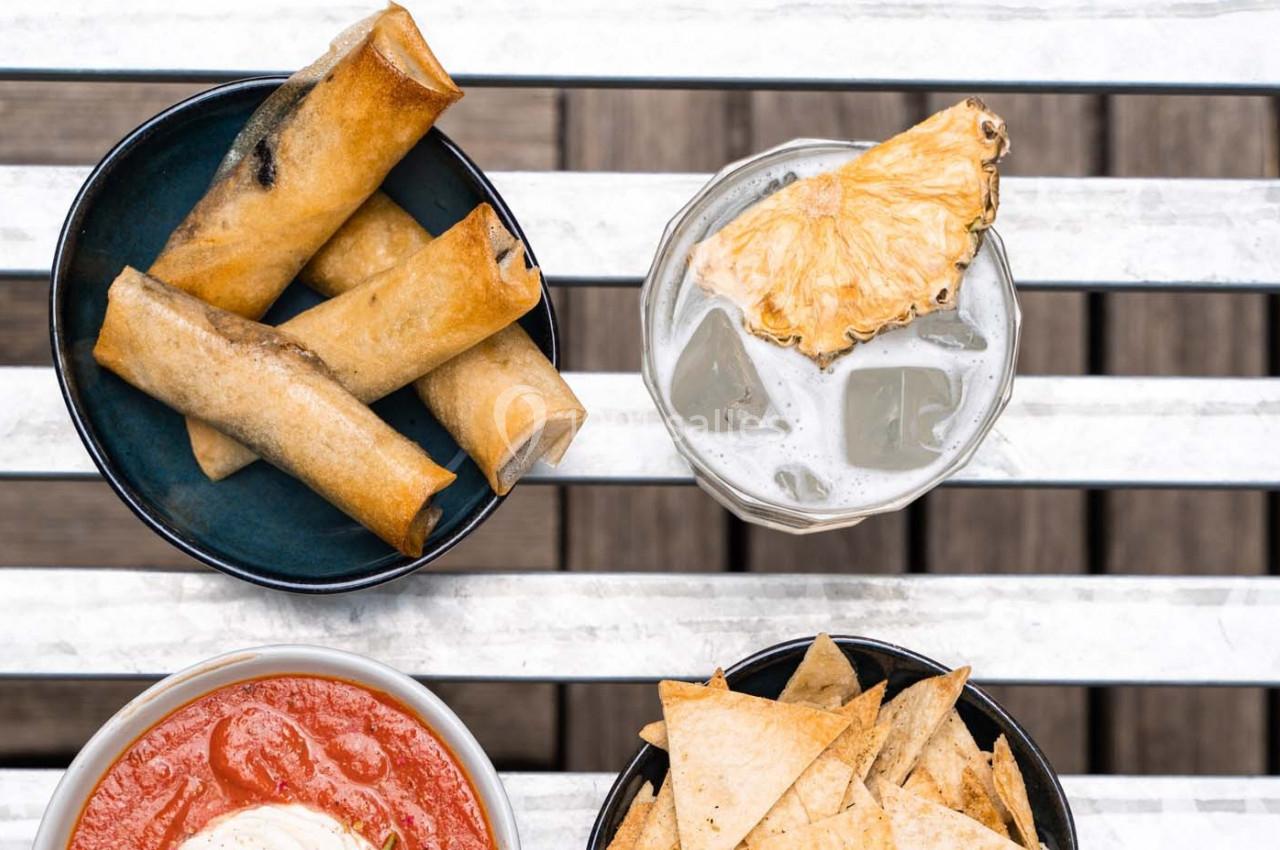 Assiette de rouleaux frits, chips avec sauce rouge, et verre de boisson glacée décoré d'une tranche d'ananas.