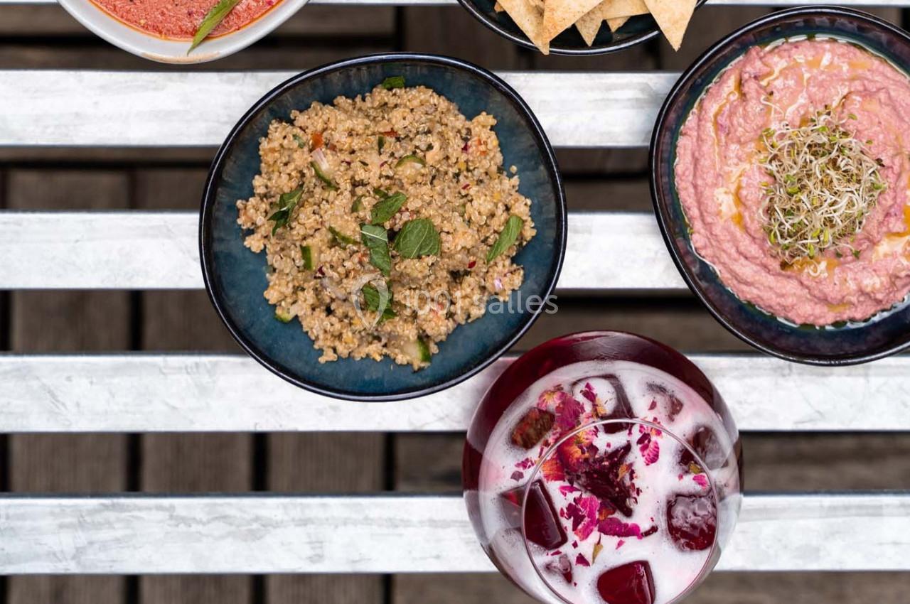 Assiette de taboulé, houmous rose et boisson garnie de betteraves et pétales, posés sur une table blanche.
