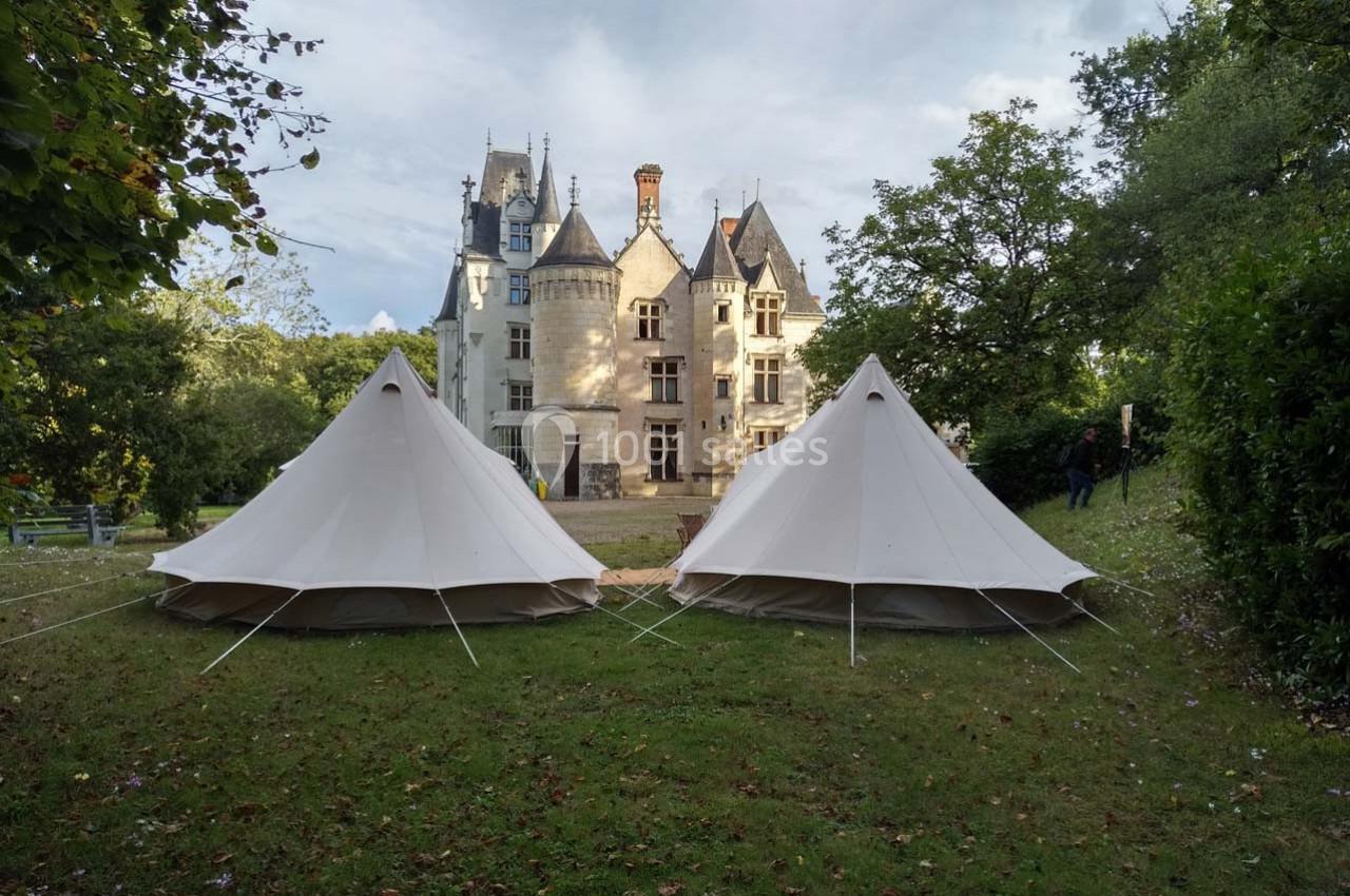 Deux tentes blanches installées sur une pelouse devant un château entouré d'arbres.