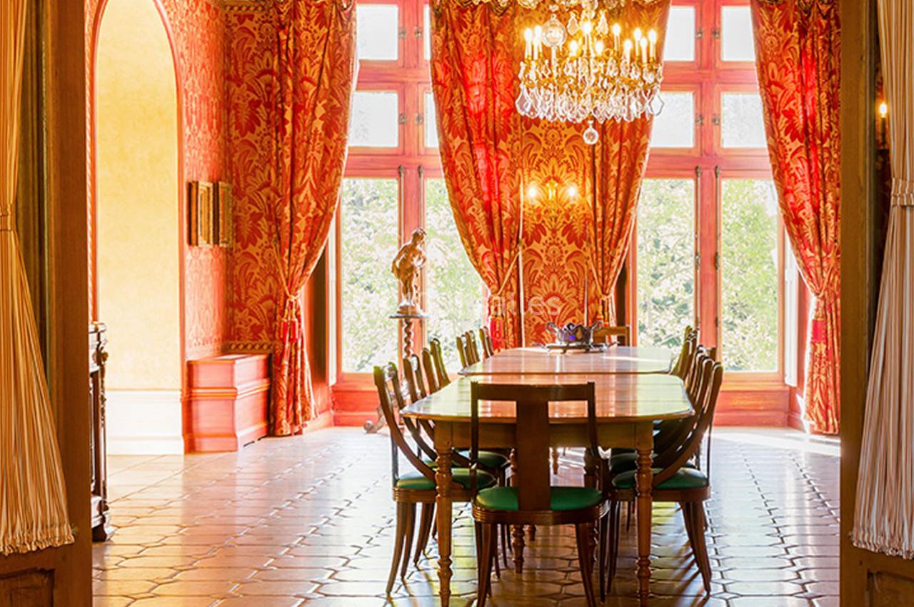 Salle à manger élégante avec une grande table en bois, chaises vertes, lustre en cristal et rideaux rouges ornés.
