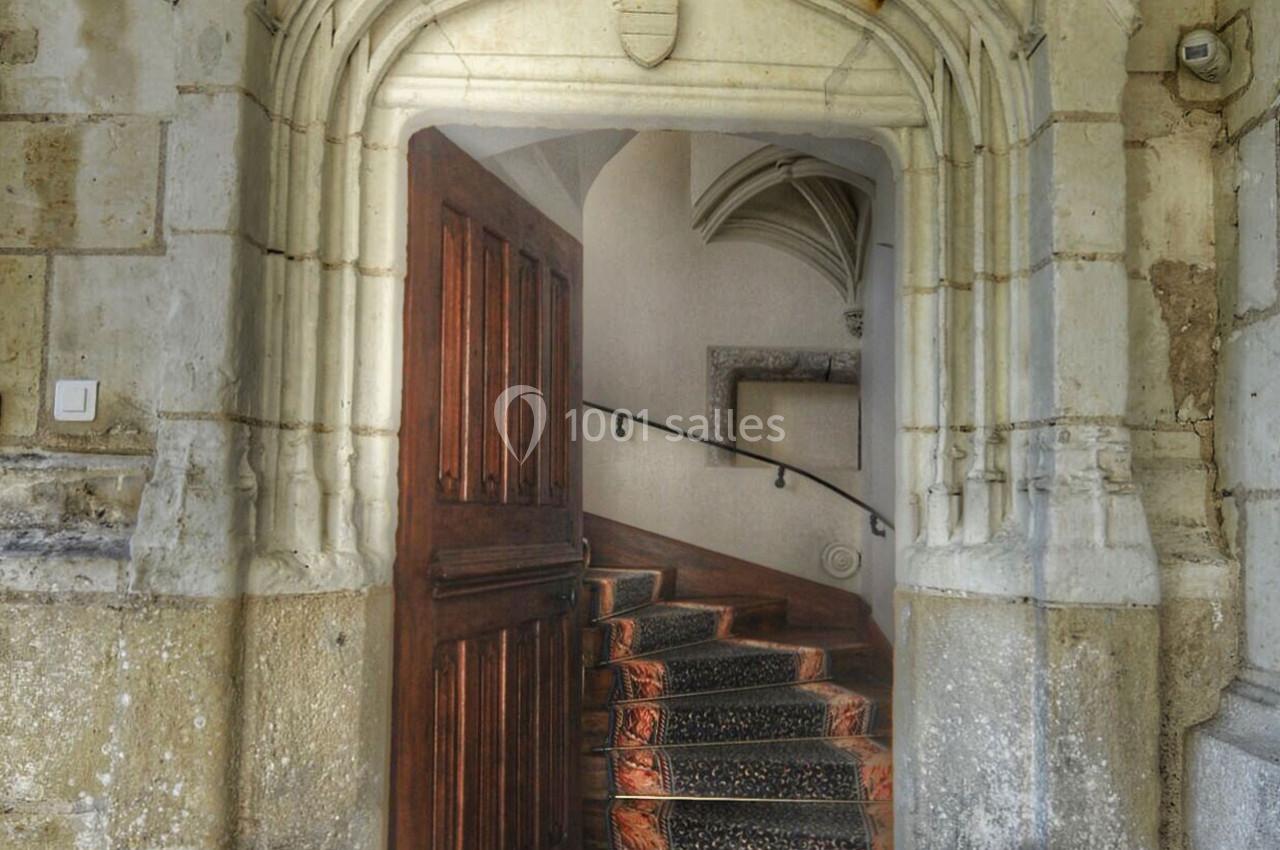 Porte en bois ouverte donnant sur un escalier en pierre avec une rampe, dans un cadre architectural ancien.