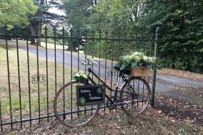 Un vélo décoré de fleurs blanches et vertes est appuyé contre une grille en fer forgé dans un cadre arboré.