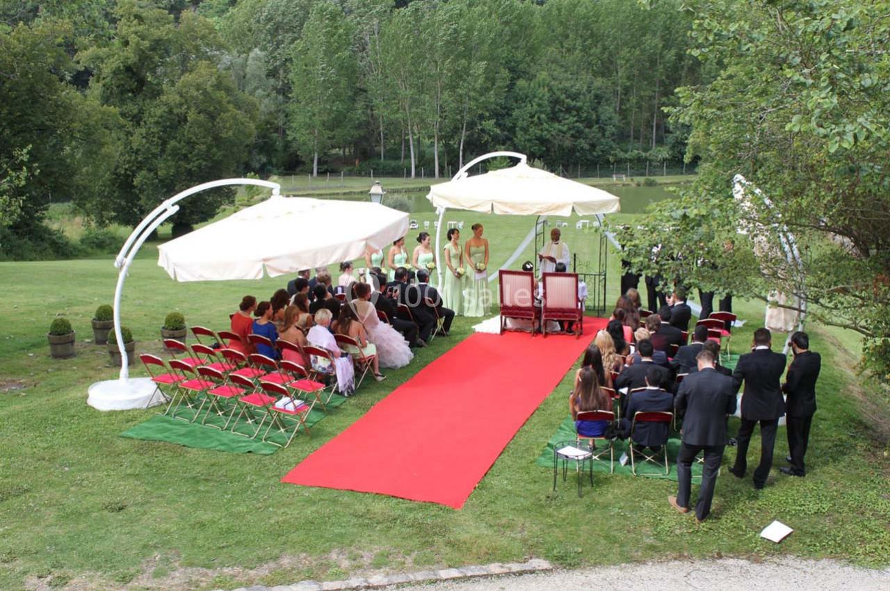 Cérémonie de mariage en plein air avec invités assis, allée rouge, et un couple sous une arche décorée.
