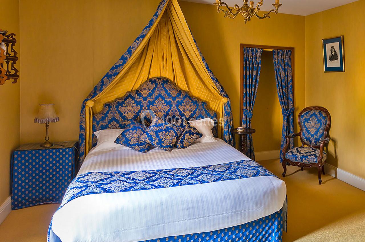 Chambre avec lit à baldaquin bleu et jaune, mobilier classique et murs peints en jaune.