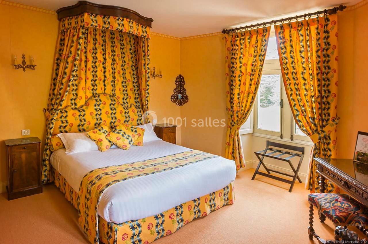 Chambre avec lit double, décorée de rideaux et textiles jaunes à motifs, éclairée par une fenêtre avec vue extérieure.