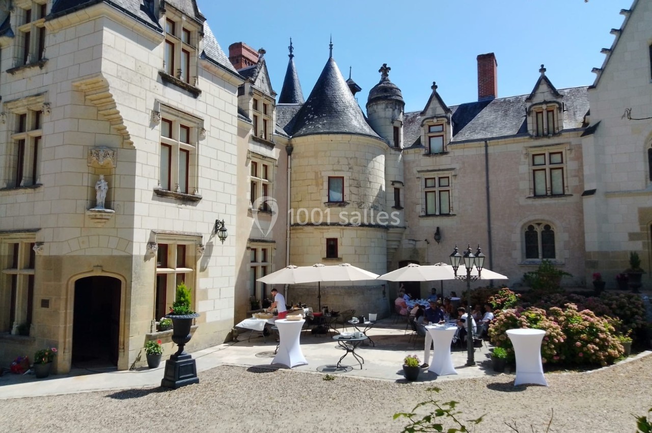 Cour intérieure d'un château avec des tables, des parasols et des personnes réunies par une journée ensoleillée.