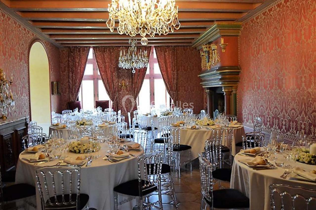 Salle de réception élégante avec tables rondes dressées, chaises transparentes et lustres en cristal.