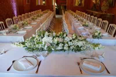 Un vélo décoré de fleurs blanches et vertes est appuyé contre une grille en fer forgé dans un cadre arboré.