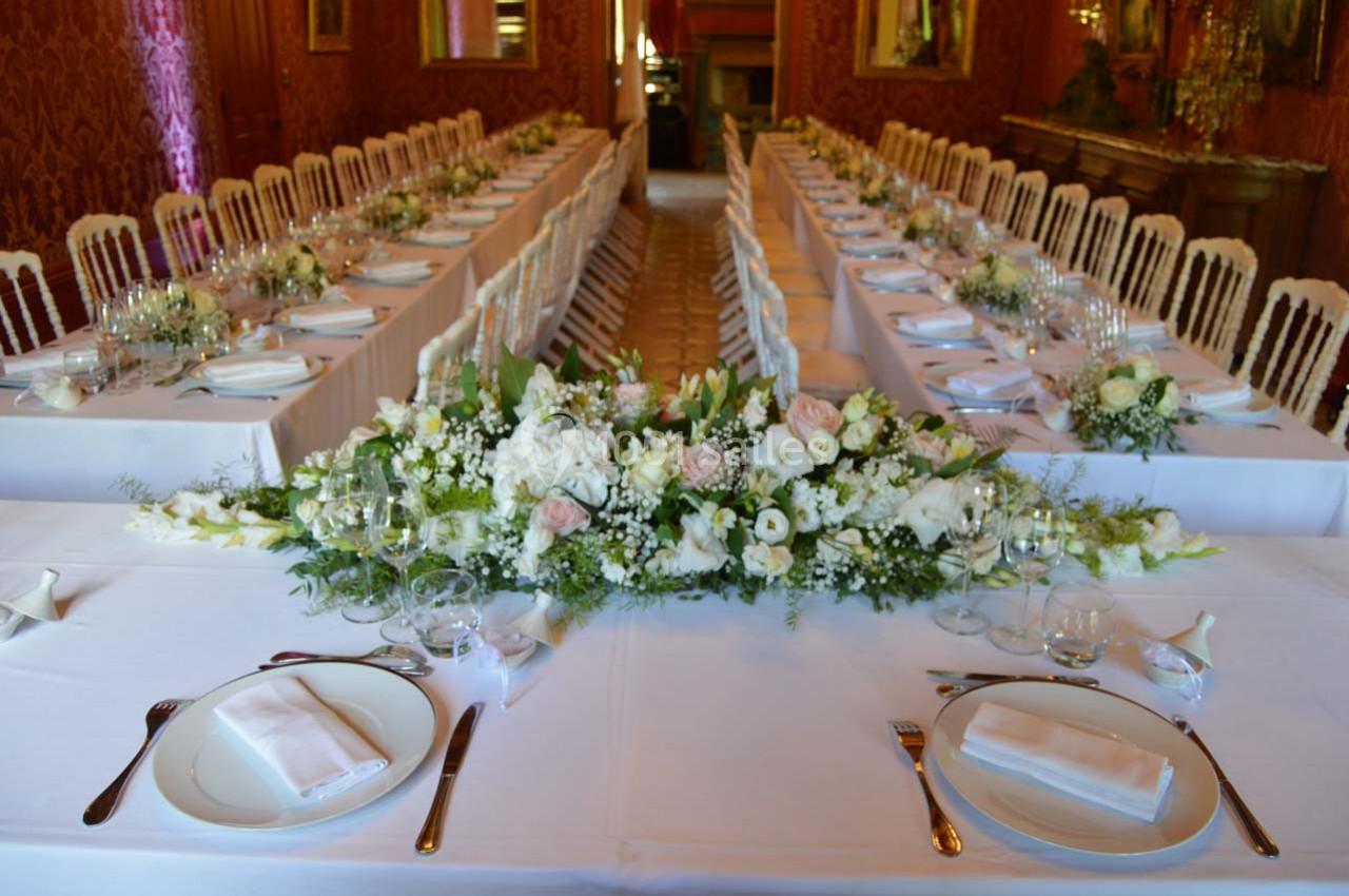 Salle de réception avec tables dressées, nappes blanches, vaisselle élégante et centre de table floral.