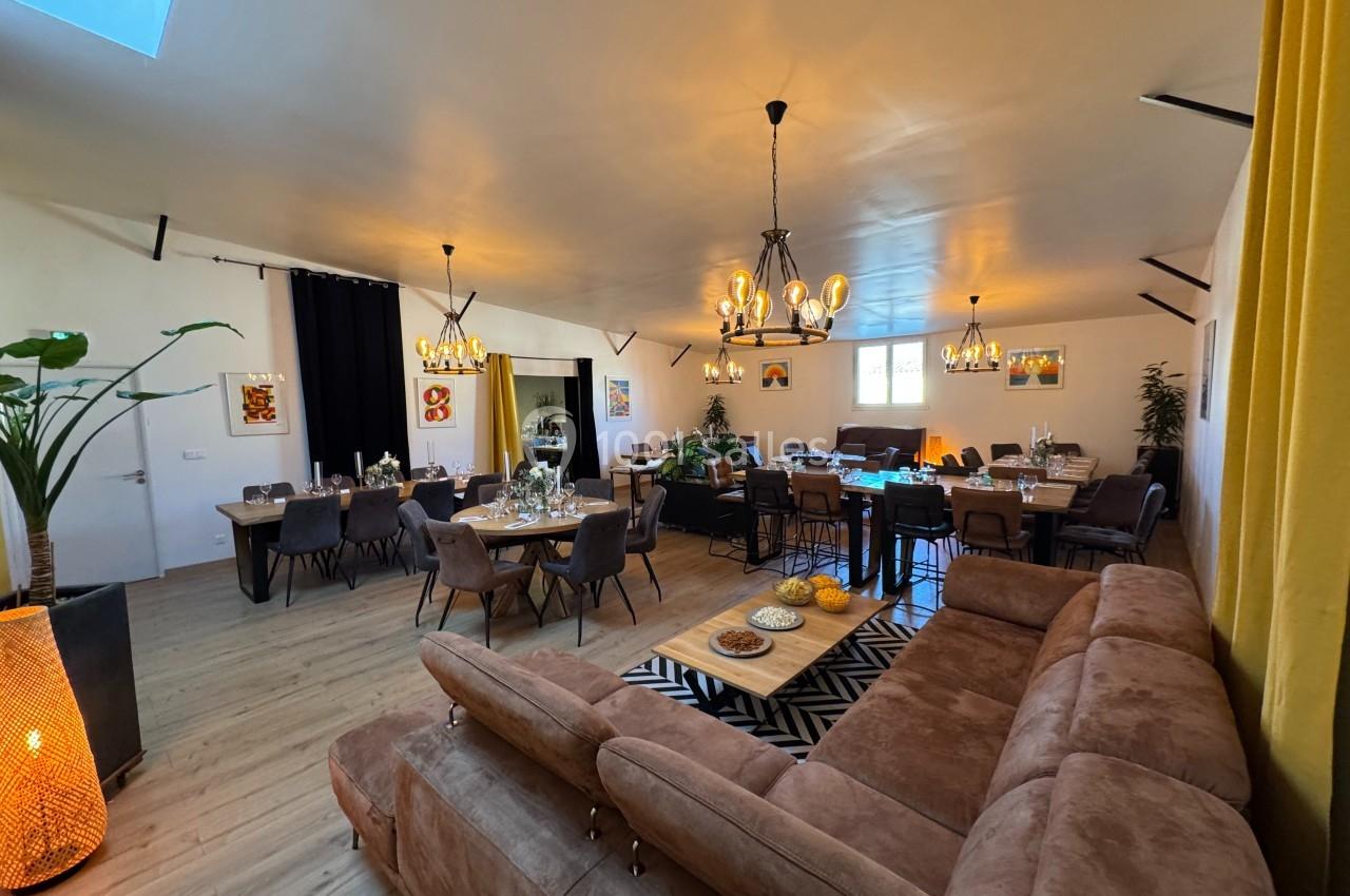 Salle lumineuse avec canapés, grandes tables dressées, suspensions décoratives et plantes en arrière-plan.