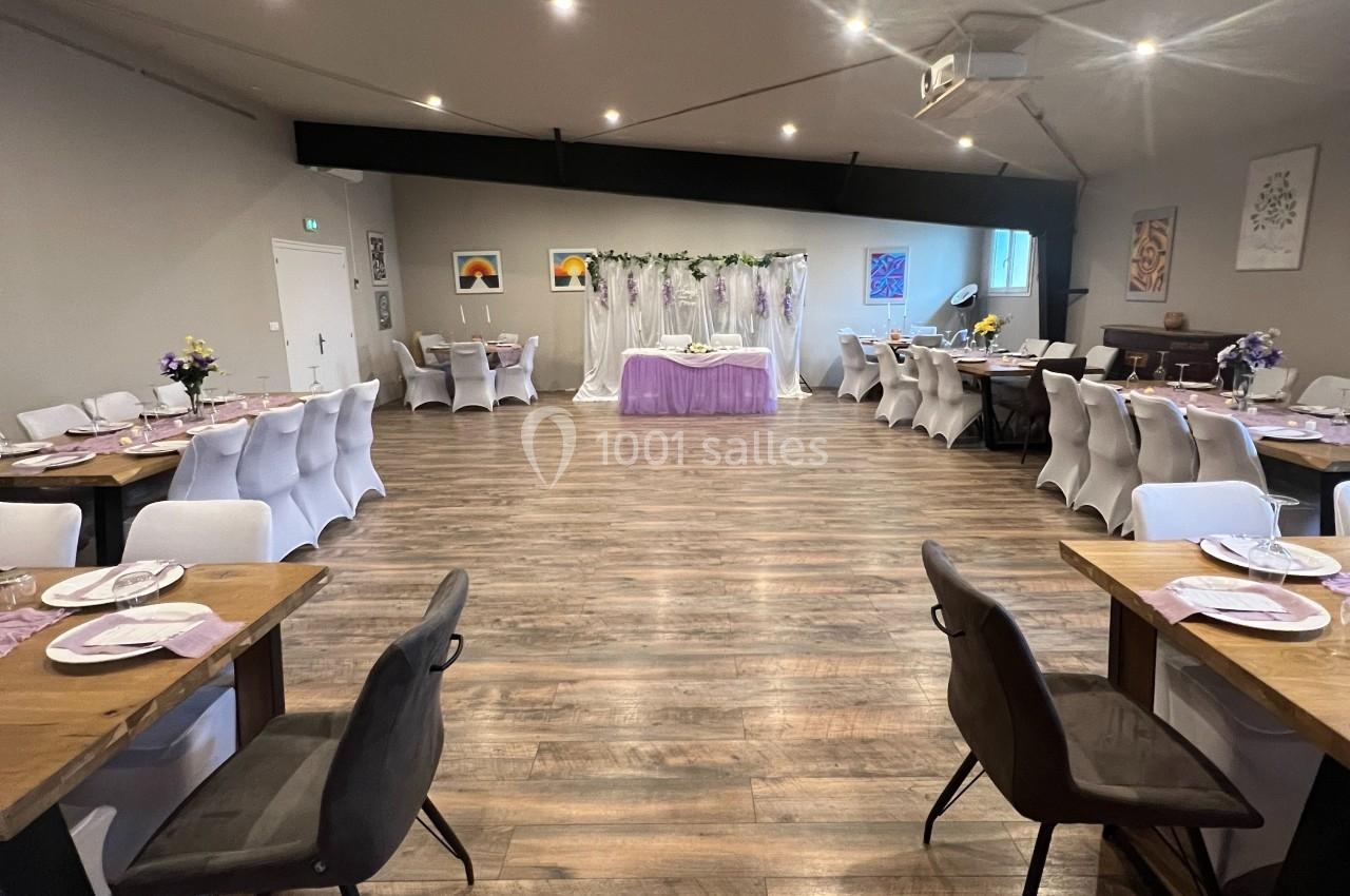 Salle de réception décorée avec des tables dressées, chaises blanches et noires, et une table centrale ornée de fleurs.