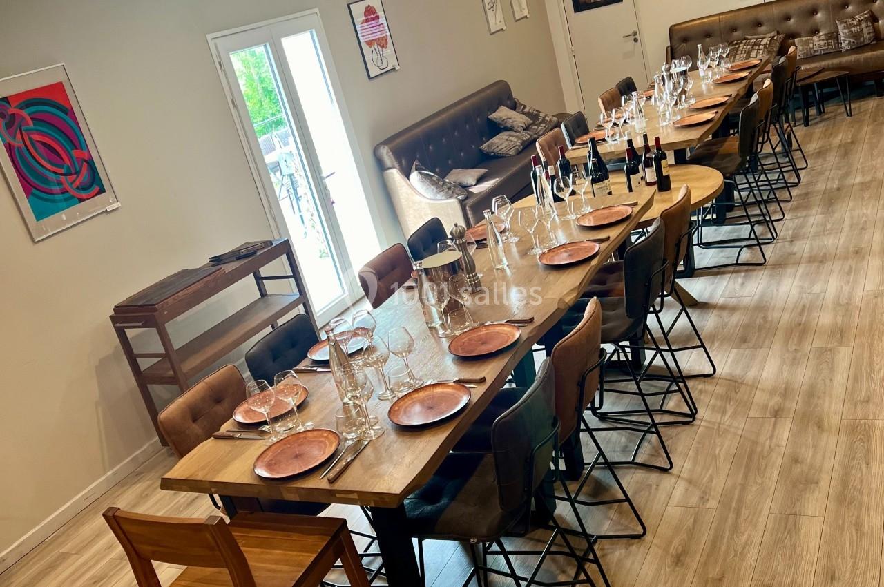 Salle lumineuse avec deux grandes tables dressées, des chaises en bois et métal, et des décorations murales modernes.