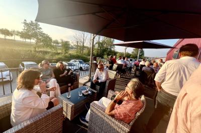 Coucher de soleil rougeoyant derrière une rangée d'arbres, vu depuis une terrasse avec mobilier et voitures garées.