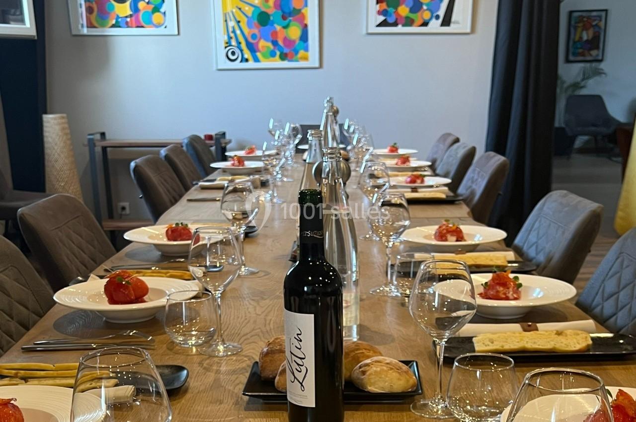 Table dressée avec assiettes contenant des entrées, couverts, verres, bouteille de vin et décorations murales colorées.