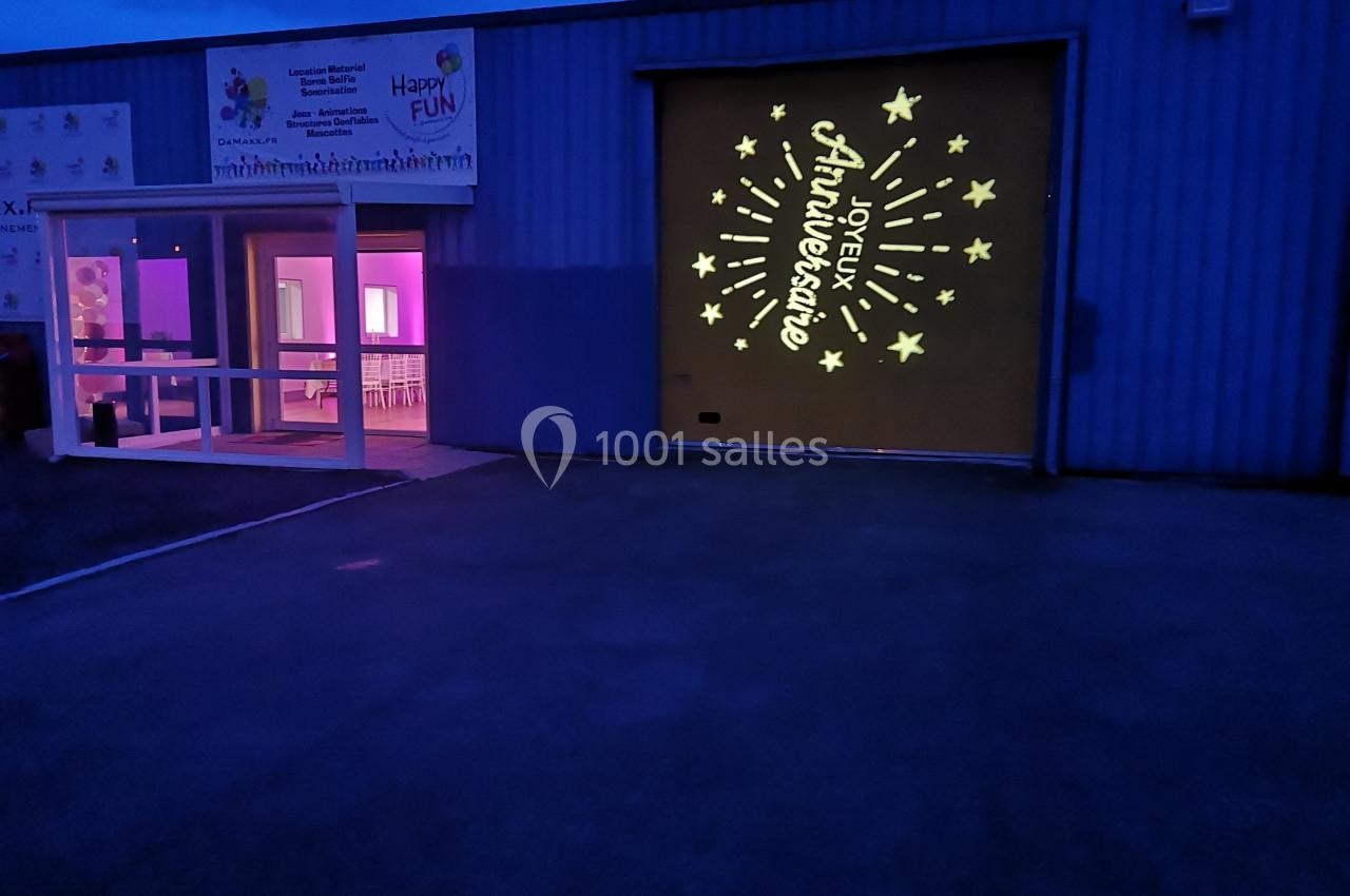 Façade d'un bâtiment éclairé avec une projection lumineuse ’Joyeux Anniversaire’ et des étoiles sur un mur.